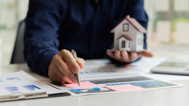 Emlakçılar müşterileri tanıtmak için evrak işleri ve ev tasarımlarıyla masalarda çalışırlar..