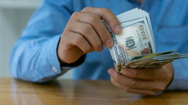 Asyalı işadamı ahşap masa üzerinde banknotlar sayıyor. Para, maaş ve şirket çalışanlarına yapılan ödemeleri sayma kavramı..