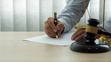 Avukat, üzerinde hakimin çekiç, altın pulları, hukuki kavramları ve danışmanları olan bir masada çalışıyor..