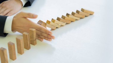 Bir işadamının eli, tahta blok bir dominonun sürekli düşmesini ya da başarılı bir müdahale stratejisini engeller. Masada yakın plan iş için fikirler var.