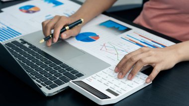 İş adamları, şirketin vergiler ve finans ile kârlı maliyetlerini analiz etmek için grafikler ve dizüstü bilgisayar hesap makineleriyle çalışıyorlar..