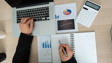 Muhasebeci elinde kalem olan bir hesap makinesi ve bilgisayar kullanıyor. Finans devam ediyor ve masraf tablosunda ve tabloda en iyi görünümlü maliye konseptiyle hesaplanıyor