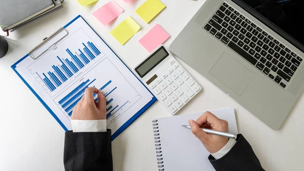 The accountant uses a calculator and a computer with a pen in hand. Finance in progress and calculated in expense table and on table with graph concept of finance with top view