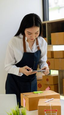 Küçük işletme girişimi, KME sahibi, Asyalı bayan girişimci okuyun ve sipariş numarasını dizüstü bilgisayara yazın. Müşterilere satılan kutuları hazırlamak için çevrimiçi siparişleri kontrol et. Çevrimiçi KOBİ iş fikri.