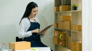 Küçük işletme girişimi, KME sahibi, Asyalı bayan girişimci okuyun ve sipariş numarasını dizüstü bilgisayara yazın. Müşterilere satılan kutuları hazırlamak için çevrimiçi siparişleri kontrol et. Çevrimiçi KOBİ iş fikri.