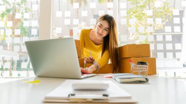 Küçük işletme girişimi, KME sahibi, Asyalı bayan girişimci okuyun ve sipariş numarasını dizüstü bilgisayara yazın. Müşterilere satılan kutuları hazırlamak için çevrimiçi siparişleri kontrol et. Çevrimiçi KOBİ iş fikri.