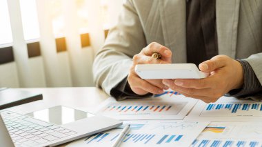 İşadamı analiz ve rehberlik için şirketin mali grafik dökümanına bakıyor. Asyalı iş adamı veya bankacı tasarruf, finans ve ekonomi kavramlarını finansal konsept dizüstü bilgisayarla hesaplıyor.