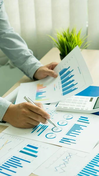 Portrait of an Asian male financial officer doing graph analysis using a calculator. Investment results reported on the desk in the office. financial accounting concept