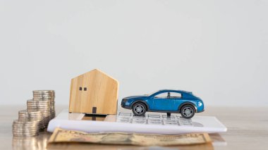 Küçük ahşap ev ve araba hesap makinesinde. Masasında bozuk para yığını var. Araba ev ödemesi konsepti..
