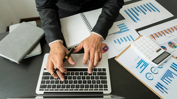 Female accountant using calculator and computer holding pen with financial graph and calculate home office expenses on top view table.