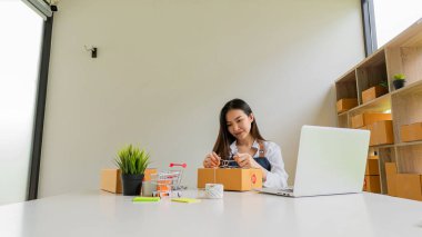 Küçük işletme girişimcisi, KOBİ, Asya 'daki küçük işletme sahibinin ofisinde kutu ve dizüstü bilgisayarı olan bağımsız, genç bir Asyalı kadın. çevrimiçi pazarlama paketleme kutusu teslimatı KOBİ-ticaret başarısı konsepti
