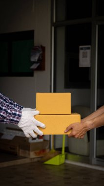 Çizgili takım elbiseli Asyalı teslimatçı evinin önünde bir karton kutu tutuyor. Ve bir adam, evin önündeki bir personelden bir kutu alır. Covid-19 salgını sırasında teslimat konsepti.