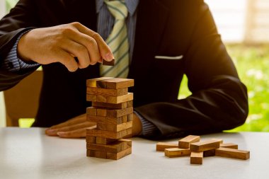 Proje yönetiminin planı, riski ve stratejisi. Bir işadamı ofisteki masadaki kuleye ahşap bir blok koyar. inşaat işi fikri