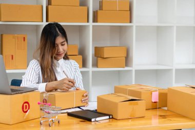 Küçük bir işletme kuran KOBİ sahipleri, Kadın Girişimciler, kutuları hazırlamak için çevrimiçi siparişleri kontrol etmek üzere kutular ve dizüstü bilgisayarlarla çalıştılar. Müşterilere satıyorum. Çevrimiçi KOBİ iş fikri.