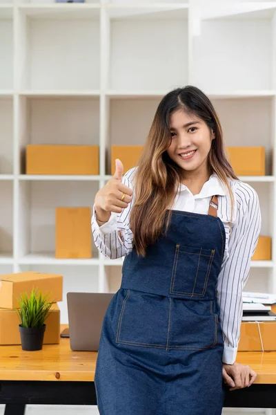 Beautiful Asian girl standing in front of the camera Business owners, startups, working happily with cardboard boxes at home Prepare to ship in SMEs, ecommerce delivery, omnichannel, online concepts.