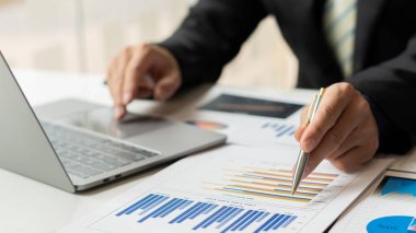 Raporlar, hesaplamalar, ev finansmanı, yatırım, ekonomi, tasarruf veya ofis sigortası fikirleri yapmak için gelir ve gider hesaplayıcıları, hesaplar veya mali denetçiler kullanarak grafik kağıtları ve dizüstü bilgisayarlar üzerinde çalışan bir işadamı.