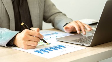 Raporlar, hesaplamalar, ev finansmanı, yatırım, ekonomi, tasarruf veya ofis sigortası fikirleri yapmak için gelir ve gider hesaplayıcıları, hesaplar veya mali denetçiler kullanarak grafik kağıtları ve dizüstü bilgisayarlar üzerinde çalışan bir işadamı.