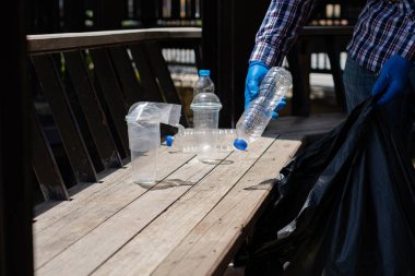 Gönüllüler hayır işi için çevresel atıkları toplamaya yardım ediyorlar. Adam plastik şişe topluyor dünyadaki çöpleri topluyor, ormanı temizliyor. Kamu bahçesinden çöp toplamaya yardım et.