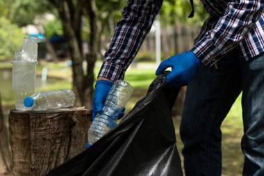 Gönüllüler hayır işi için çevresel atıkları toplamaya yardım ediyorlar. Adam plastik şişe topluyor dünyadaki çöpleri topluyor, ormanı temizliyor. Kamu bahçesinden çöp toplamaya yardım et.