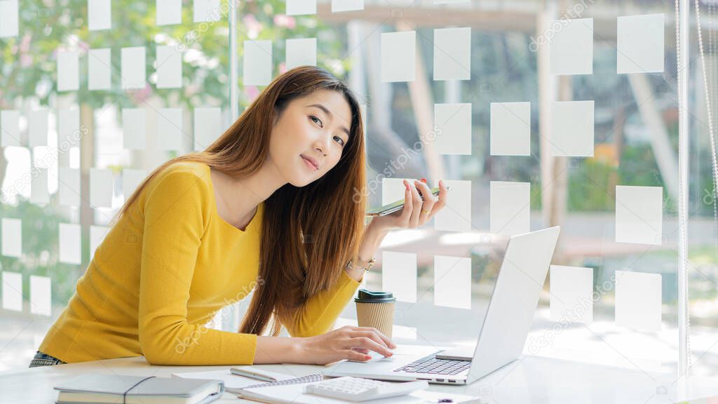 Young woman working in a coffee shop with laptop and calculator, notebook on table and phone in hand, financial business concept.