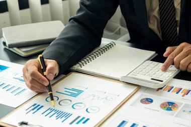 Bir analiz grafiğine, yatırım planına, iş projelerine ve iş tartışma stratejilerine işaret eden bir kalem tutan işadamı.