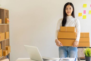 Evde internet üzerinden çalışan genç iş kadını. Kadın işadamları evde çalışmak ve KOBİ işine başlamak için dizüstü bilgisayar kullanıyorlar. İş yerinde küçük ve karton kutular var.