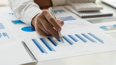 Masa başında ofis masraflarını hesaplayan ve para kazanan eller. Bir muhasebeci, bir grafik belgesini gösteren bir kalem tutan bir hesap makinesi ve bilgisayar kullanır..