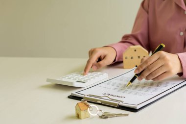 İş adamı veya ev satış temsilcisi, satış ve kira için faiz, vergi ve kârı hesaplamak için sözleşme belgeleri ve dizüstü bilgisayarla çalışır..