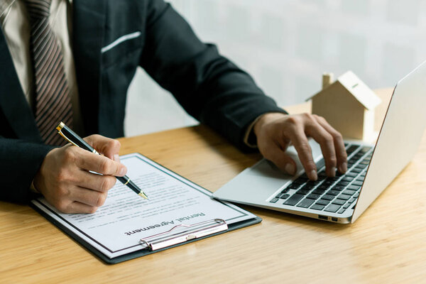 Businessman or home sales representative works with contract documents and calculator with laptop To calculate interest, taxes and profits for sale and rent.