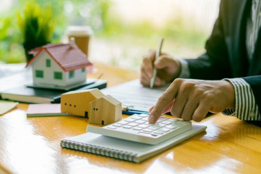 İş adamı ya da ev satış temsilcisi, iş yerinde sözleşmeli belgeler ve dizüstü bilgisayarlı hesap makinesiyle çalışan iş adamı ya da ev satış temsilcisi olarak çalışır. faiz, vergi ve karı hesaplamak için