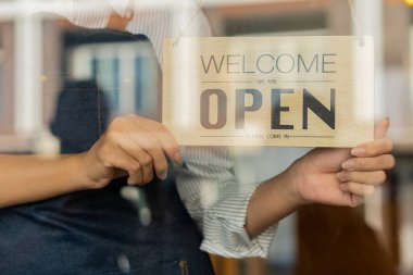 Bir kafe ya da restoranın sahibi küçük bir işletme dükkanının giriş kapısına açık bir tabela asar. Dükkan sahibi cam kapıdan tabelayı ardına kadar açtı ve servis yapmaya hazırdı..