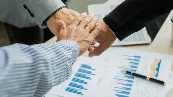 business people join hands to work as a team of business mergers and successful negotiations 3 business people join hands with partners to celebrate partnership and business deal idea in office and on the table with graphs.