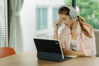 Genç ve güzel bir Asyalı serbest yazar bir şey düşünüyor, tablet ekrana bakıyor ve kafasına dokunuyor..