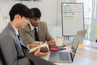 Bir grup iş adamı bir proje veya sunum üzerinde birlikte çalışarak dizüstü bilgisayar, belge ve kahve ile toplantı yapıyor veya tartışıyorlar, bir beyin fırtınası veya proje planlama faaliyeti öneriyorlar.