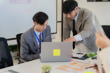 Bir grup iş adamı bir proje veya sunum üzerinde birlikte çalışarak dizüstü bilgisayar, belge ve kahve ile toplantı yapıyor veya tartışıyorlar, bir beyin fırtınası veya proje planlama faaliyeti öneriyorlar.