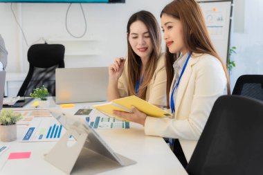 İki iş kadını mali tabloları ve grafikleri incelerken, modern ofiste strateji ve pazar analizlerini tartışırken, profesyonel kadın da mali tablolara bakıyor..