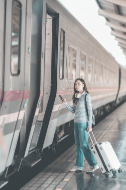 Güzel Asyalı bir kadın, elinde defteriyle tren istasyonundaki ahşap bankta dinleniyor. Sırt çantasıyla tren bekliyor. Seyahat yaşam tarzının tadını çıkarıyor..