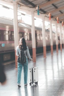 Sırt çantalı Asyalı kadın tren istasyonunda bavulunu tutarken, trenin hareket etmesini beklerken, yolculuk için heyecanlıydı..