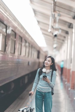 Sırt çantalı Asyalı kadın tren istasyonunda bavulunu tutarken, trenin hareket etmesini beklerken, yolculuk için heyecanlıydı..