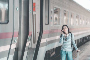 Sırt çantalı Asyalı kadın tren istasyonunda bavulunu tutarken, trenin hareket etmesini beklerken, yolculuk için heyecanlıydı..