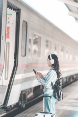 Sırt çantalı Asyalı kadın tren istasyonunda bavulunu tutarken, trenin hareket etmesini beklerken, yolculuk için heyecanlıydı..