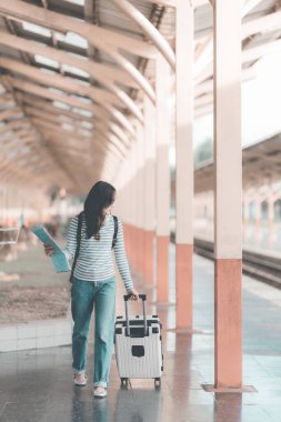 Sırt çantalı Asyalı kadın tren istasyonunda bavulunu tutarken, trenin hareket etmesini beklerken, yolculuk için heyecanlıydı..