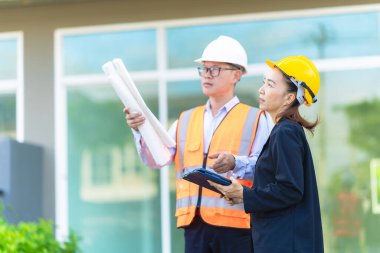 Asyalı erkek ve kadın mühendislerden oluşan bir ekip bina planlarına, inşaat mühendisliğine, iç teftişe ve konut geliştirme çalışmalarına göre bir binanın yapısını inceliyor..