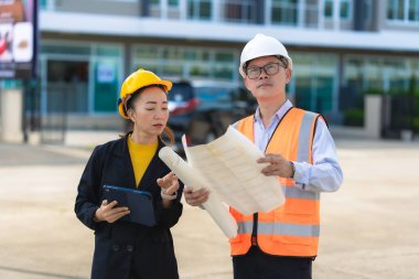 Asyalı erkek ve kadın mühendislerden oluşan bir ekip bina planlarına, inşaat mühendisliğine, iç teftişe ve konut geliştirme çalışmalarına göre bir binanın yapısını inceliyor..
