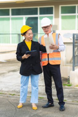 Asyalı erkek ve kadın mühendislerden oluşan bir ekip bina planlarına, inşaat mühendisliğine, iç teftişe ve konut geliştirme çalışmalarına göre bir binanın yapısını inceliyor..