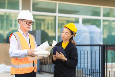 Asyalı erkek ve kadın mühendislerden oluşan bir ekip bina planlarına, inşaat mühendisliğine, iç teftişe ve konut geliştirme çalışmalarına göre bir binanın yapısını inceliyor..