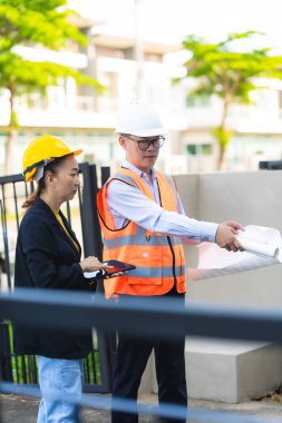 Asyalı erkek ve kadın mühendislerden oluşan bir ekip bina planlarına, inşaat mühendisliğine, iç teftişe ve konut geliştirme çalışmalarına göre bir binanın yapısını inceliyor..