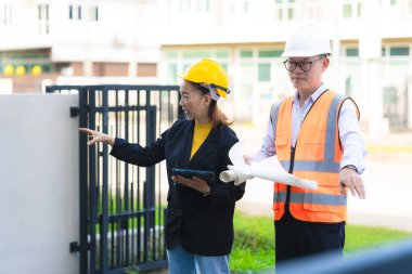 Asyalı erkek ve kadın mühendislerden oluşan bir ekip bina planlarına, inşaat mühendisliğine, iç teftişe ve konut geliştirme çalışmalarına göre bir binanın yapısını inceliyor..