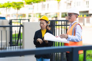 Asyalı erkek ve kadın mühendislerden oluşan bir ekip bina planlarına, inşaat mühendisliğine, iç teftişe ve konut geliştirme çalışmalarına göre bir binanın yapısını inceliyor..
