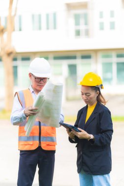 Asyalı erkek ve kadın mühendislerden oluşan bir ekip bina planlarına, inşaat mühendisliğine, iç teftişe ve konut geliştirme çalışmalarına göre bir binanın yapısını inceliyor..